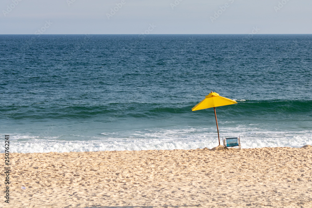 yellow sun umbrella and chair on a beautiful sunny day on the beach with the clear blue sea in the background