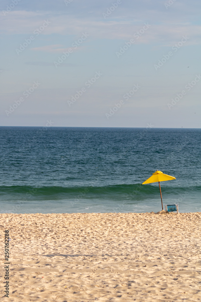 yellow sun umbrella and chair on a beautiful sunny day on the beach with the clear blue sea in the background