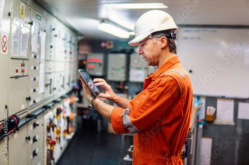 Marine chief engineer watching digital tablet in engine control room. Internet and home connection at sea.