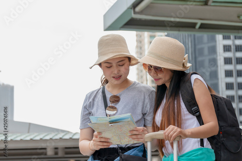 Two beautiful women travel together on a holiday. They smile happy and enjoy the urban environment.