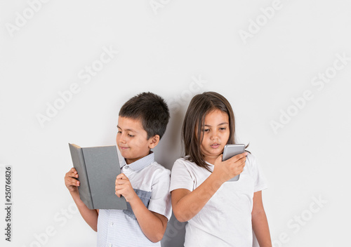 Young boy reading a book and a young girl looking at a phone.