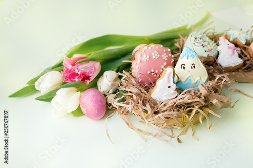 Colorful Easter cookies with frosting icing decor, painted colorful eggs and tulips on light table. Springtime holiday concept, greeting background with copy space, traditional food photo