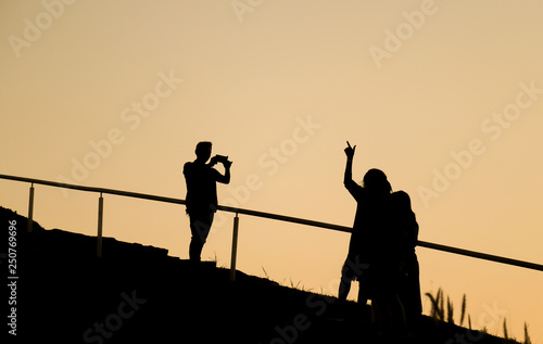 Silhouette image of lovely Asian family action, father taking photo of mother and daughter during walking up the hill in twilight evening for recreation. 