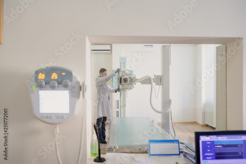 the picture of a male radiologist adjusting the X-ray machine behind the screen