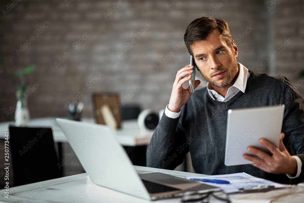 Businessman talking on the phone while using wireless technology at work. Businessman talking on the phone while using wireless technology at work.