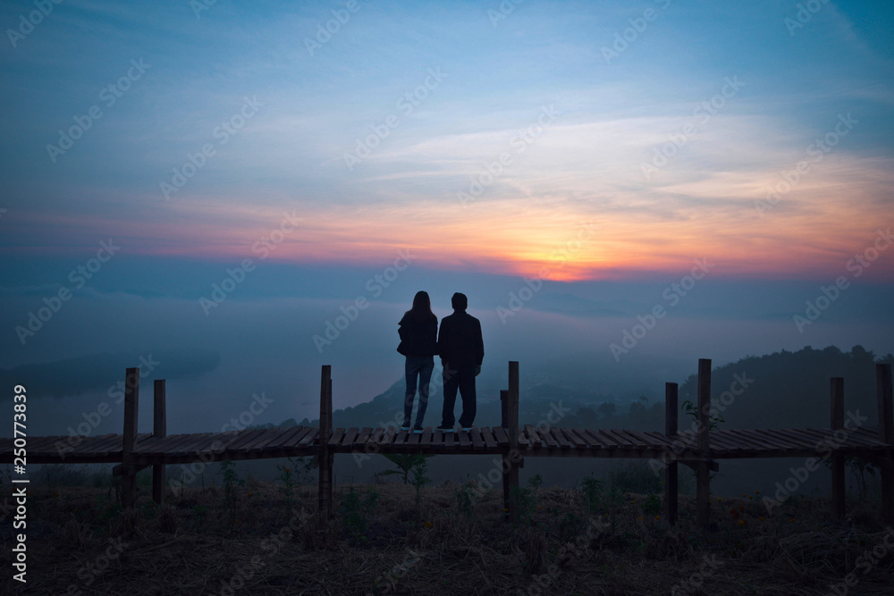 View on hill lover couple silhouette standing on a wooden bridge