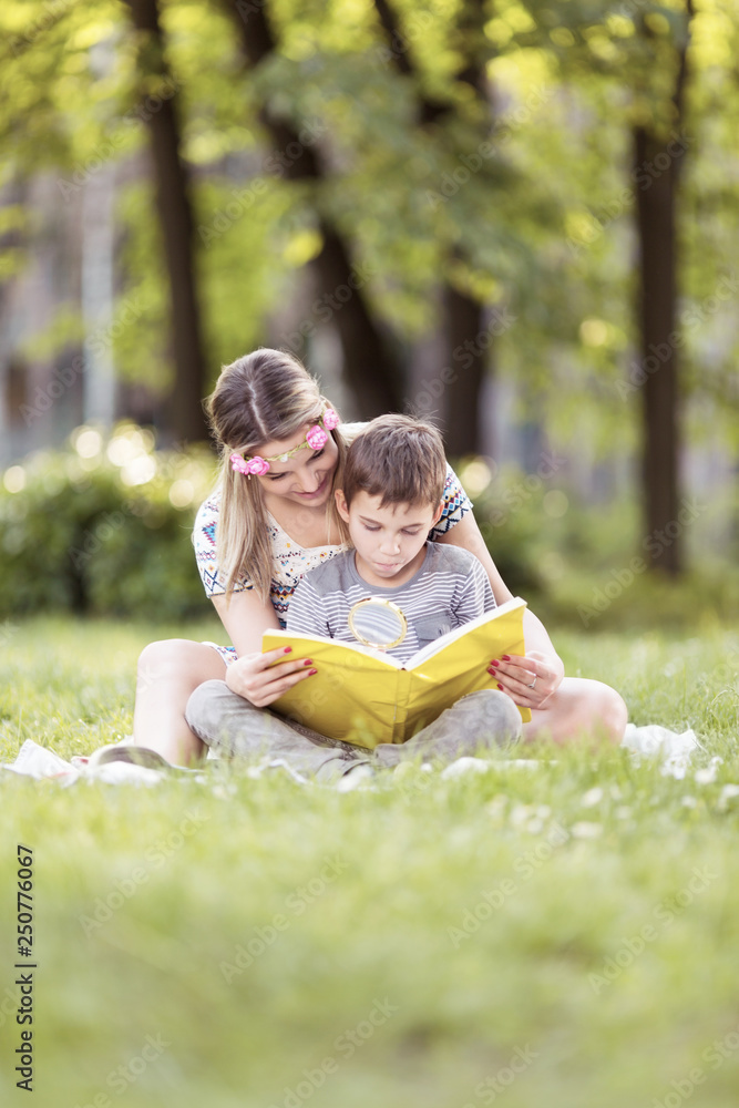 Mother and son sitting on a grass in park and reading a book