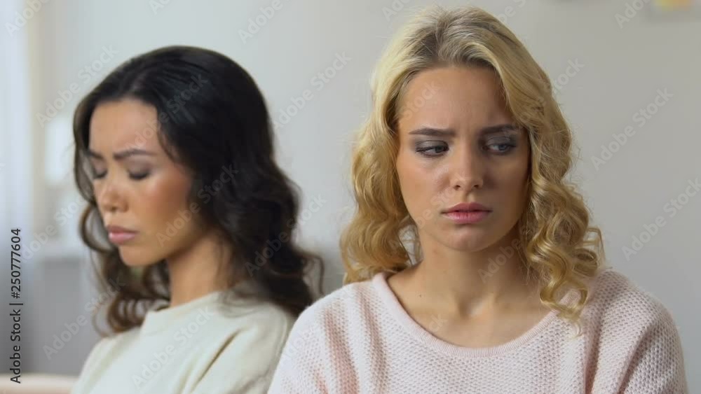 Two offended women sitting separately on couch glancing at each other, quarrel Two offended women sitting separately on couch glancing at each other, quarrel