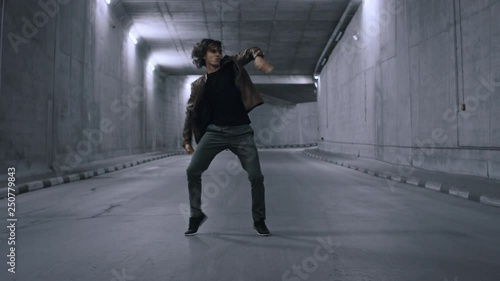 Serious Cool Young Hipster Man with Long Hair is Energetically Dancing Hip Hop in a Lit Concrete Tunnel photo