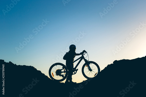 Silhouette of a little girl with a bicycle at sunset