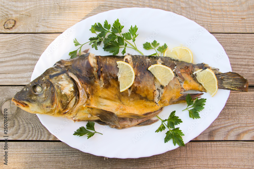 Tasty baked carp in white plate on wooden table. Top view Tasty baked carp in white plate on wooden table. Top view