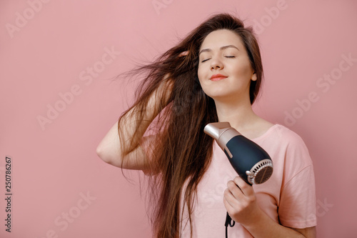 young woman makes hair volume with  hairdryer in hand on pink background photo