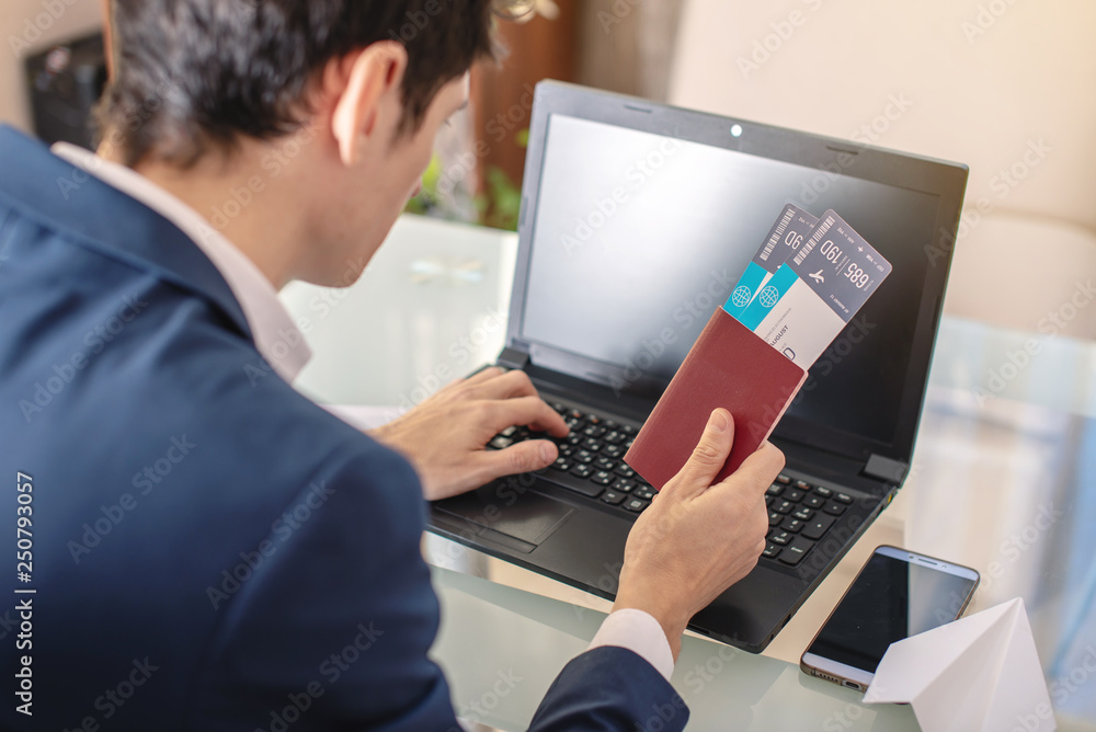 Businessman holding airline ticket and passport buying on the Internet using a laptop. Purchasing and booking online