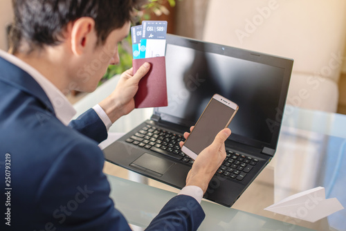 Businessman holding airline ticket and passport buying on the Internet using a laptop. Purchasing and booking online © Artem