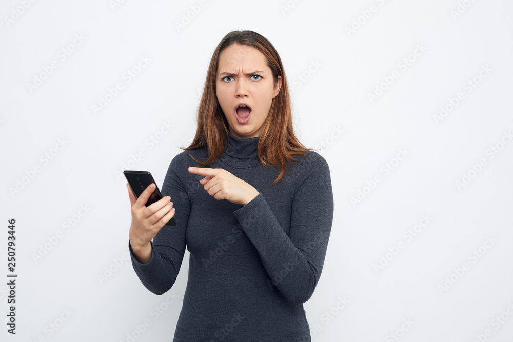 Naklejka premium portrait of surprised young woman pointing at mobile phone