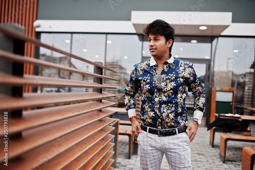 Attractive and handsome stylish indian man wear on shirt, holding mobile phone and standing in the terrace of modern lounge cafe at his work break.