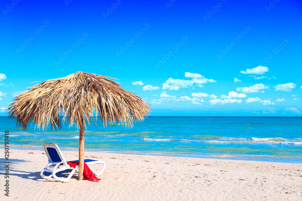 A sun lounger under an umbrella on the sandy beach by the sea and cloudy sky. Vacation background. Idyllic beach landscape. Free space for your text