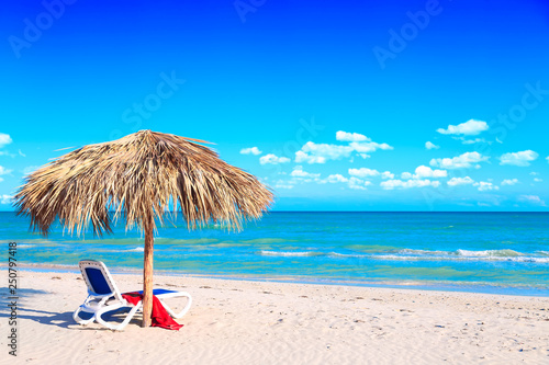 Fototapeta A sun lounger under an umbrella on the sandy beach by the sea and cloudy sky