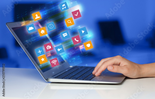 Hand using laptop with colorful fast moving application icons and symbols concept
