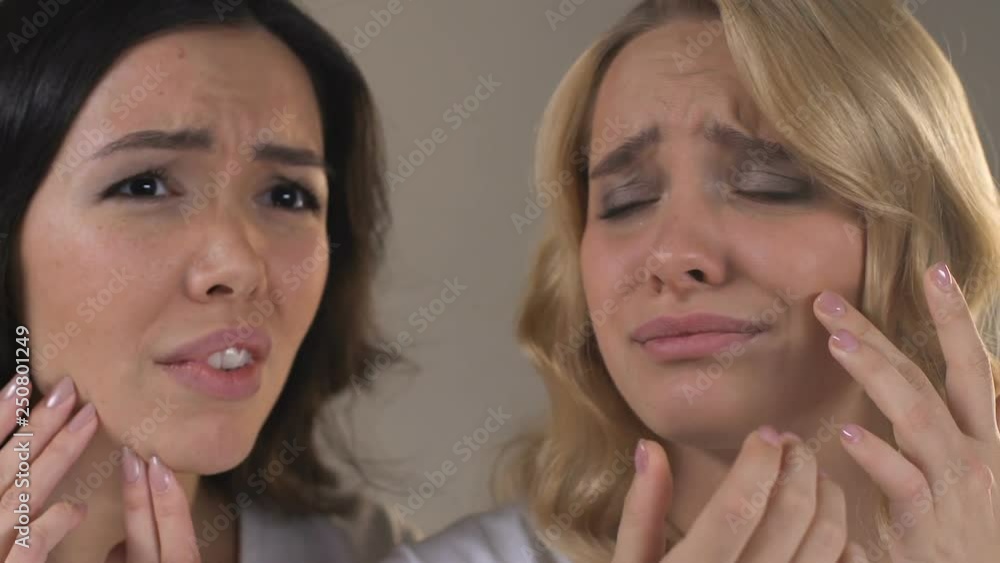 Girls examining in mirror acne and redness on skin, poor quality cosmetics Girls examining in mirror acne and redness on skin, poor quality cosmetics