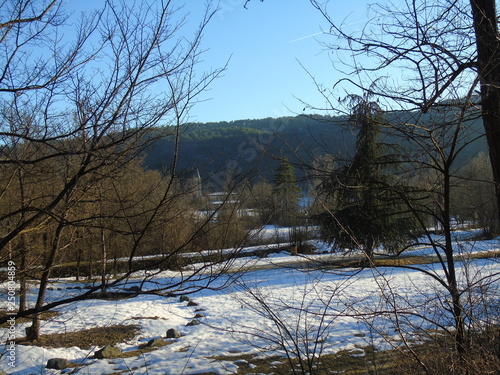 Tiglieto  Italy - 02 19 2019  Beautiful blue background of the first snow in the village in winter with some beautiful snow on the ground and sunshine over the tall trees.