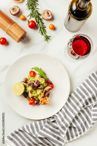 top view of salad on white plate with glass and bottle of wine and cloth