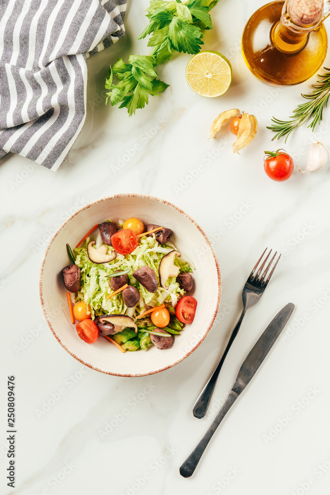 salad on white bowl with bottle of oil, cherry tomatoes, lime and rosemary on table salad on white bowl with bottle of oil, cherry tomatoes, lime and rosemary on table