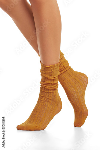 Cropped shot of lady's legs wearing pair of ochre-colored lace loose socks, standing on tiptoe against the white background. Leg-wear with stylish ornament. Fashionable legwear for voguish ladies.