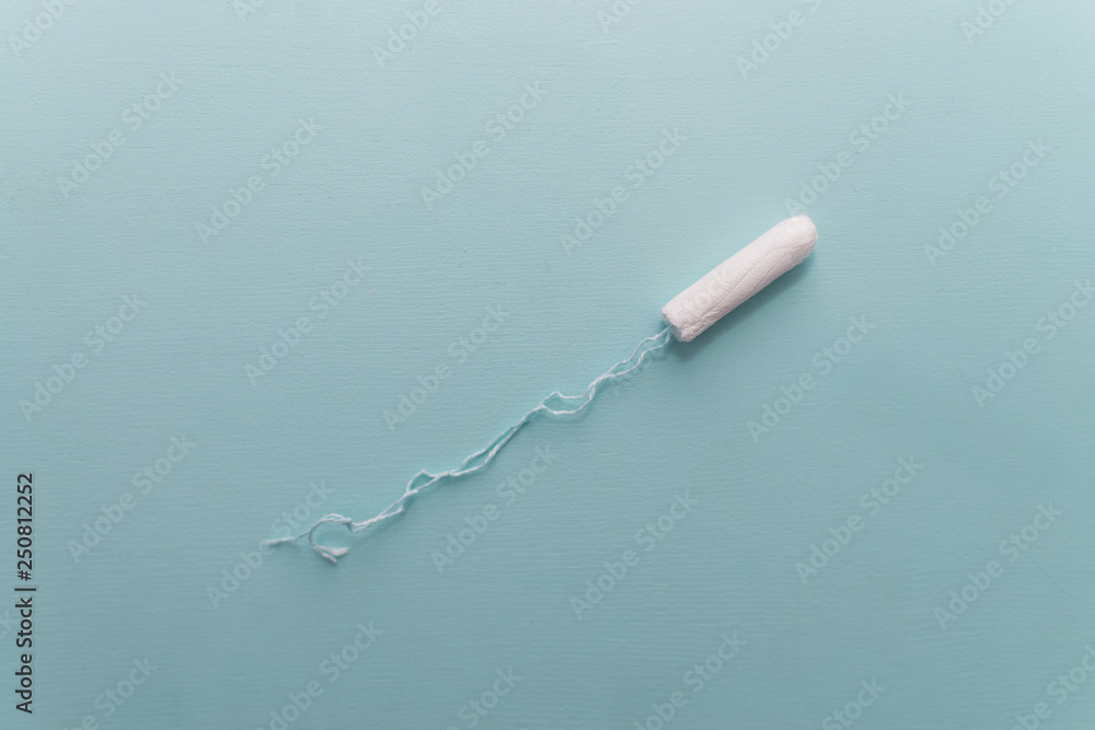 One white tampon with selective focus and empty space for text or image on blue background. Woman hygiene for period days, menstrual mothly cycle. Protective care for woman health. One white tampon with selective focus and empty space for text or image on blue background. Woman hygiene for period days, menstrual mothly cycle. Protective care for woman health.