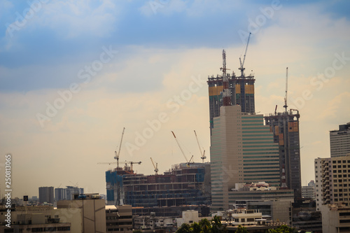 Large-scale construction site with tower cranes to erect high-rise buildings against blue sky and cloudy background.