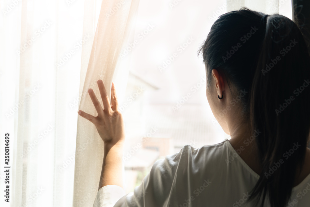 sad woman holding the curtains open to look out of a large light window at home, interior sad woman holding the curtains open to look out of a large light window at home, interior