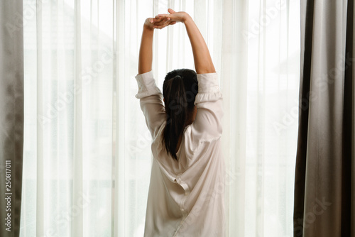 Woman stretching in bedroom after wake up, back view