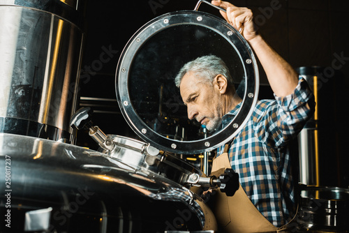 professional male brewer in working overalls checking brewery equipment photo