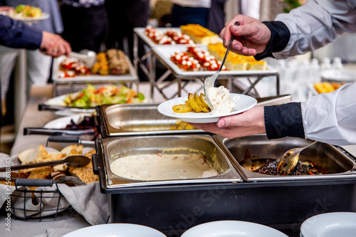 waiter's hands are putting potatoes and chicken meat in a sauce on a plate at catering event on some festive event, party or wedding reception