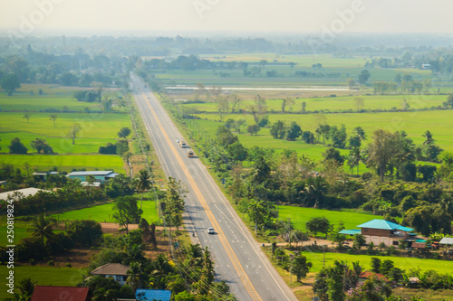 Aerial view over highway from hilltop around with countryside green rice fields and blue sky background. The provincial highway with cars and trucks crossing the hills at Phichit province, Thailand.