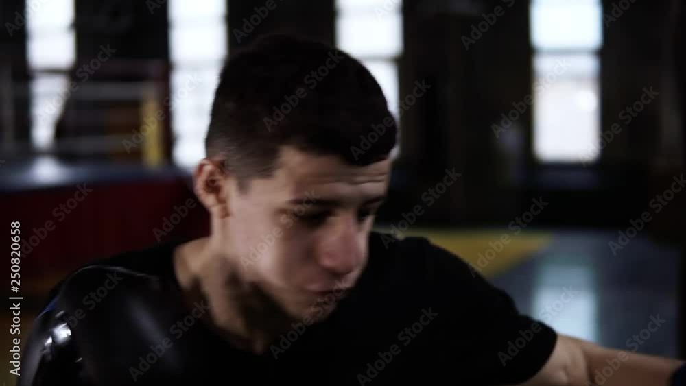 Man in black T-shirt, determinated boxer making strikes on a boxing bag indoor in the gym. Fighter training alone in slow motion Man in black T-shirt, determinated boxer making strikes on a boxing bag indoor in the gym. Fighter training alone in slow motion