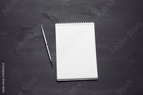 Blank notepad with a pen on black wooden desk. Top View