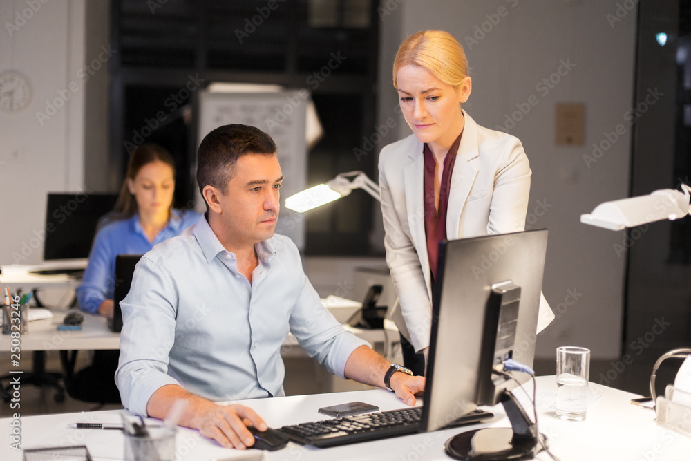 business, deadline and technology concept - coworkers with computer working late at night office