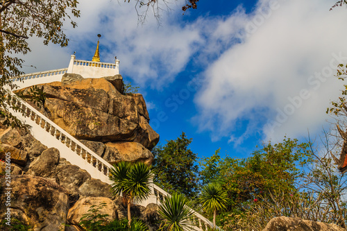 Stair way upward to the golden pagoda on the hill with blue sky background at Wat Khao Rup Chang or Temple of the Elephant Hill, one of the most famous attractions in Phichit province, Thailand. photo