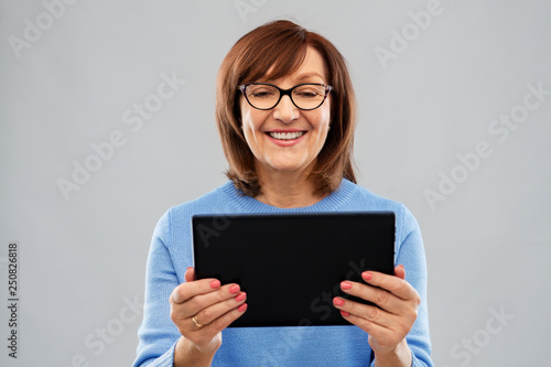 technology and old people concept - smiling senior woman in glasses using tablet computer over grey background