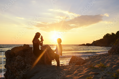 Mother and son playing on the beach at the sunset time. Concept of family life and summer vacations