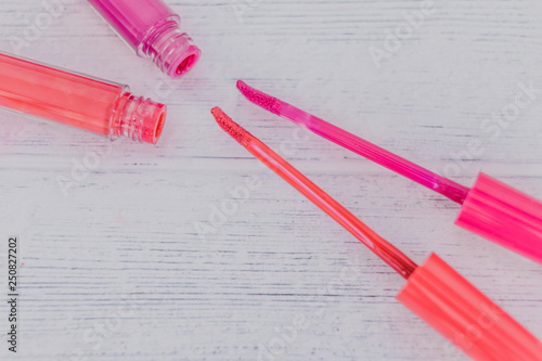 close-up of pink and orange lipglosses or liquid lipsticks on light wooden table photo