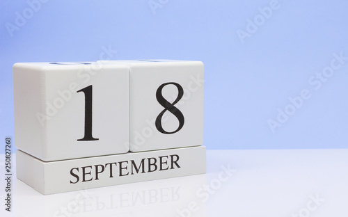 September 18st. Day 18 of month, daily calendar on white table with reflection, with light blue background. Autumn time, empty space for text