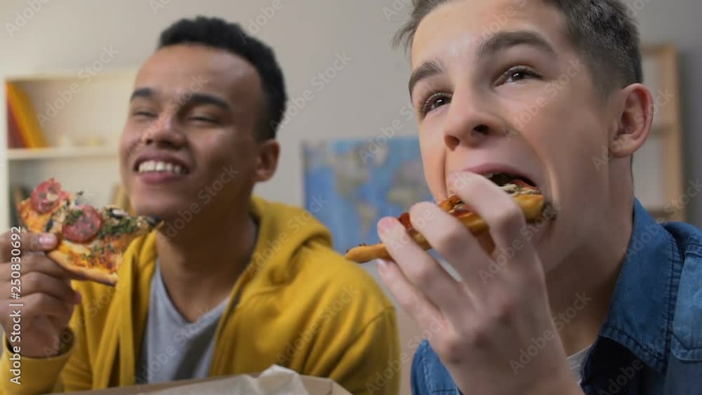 Two friends laughing, watching sitcom comedy series on tv while eating pizza