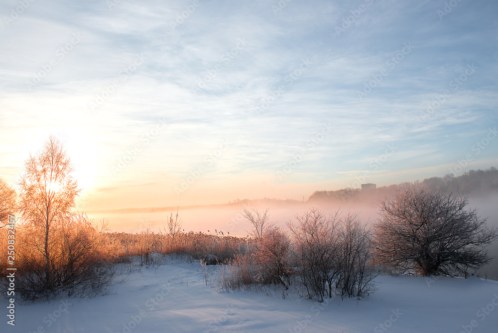 wonderful winter scene. Frosty, misty morning on the small river. frost covered trees in the warm glow of sunrise on the beach. The beauty of the world