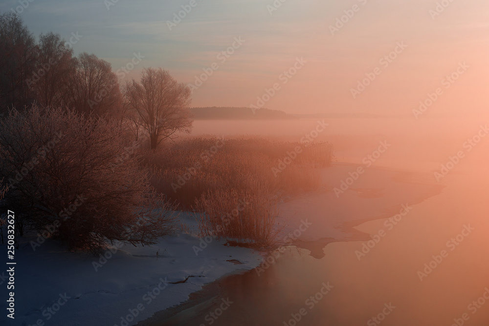 wonderful winter scene. Frosty, misty morning on the small river. frost covered trees in the warm glow of sunrise on the beach. The beauty of the world