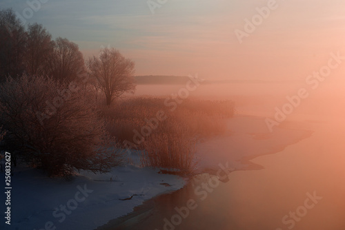 wonderful winter scene. Frosty, misty morning on the small river. frost covered trees in the warm glow of sunrise on the beach. The beauty of the world