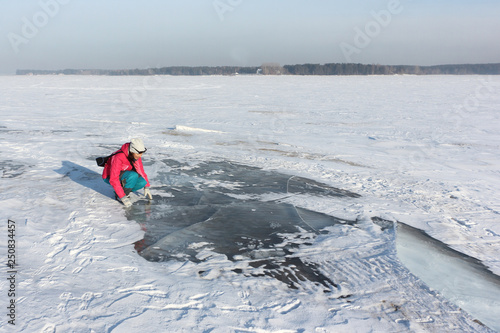 Woman in a red jacket examines the transparent ice on the river, Ob reservoir, Siberia, Russia