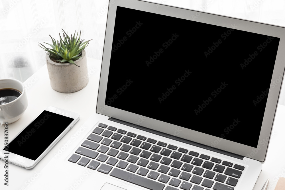 Fototapeta premium Laptop computer and smartphone with blank mock up screens are on top of white office desk table.