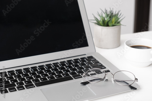 Eye glasses is put over a laptop on white office desk table with cup of coffee and office supplies.